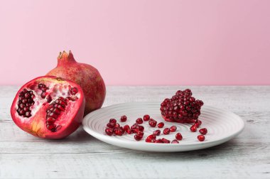 Nar bütün, yarısı ve tohumlar beyaz tabağa saçılmış, beyaz rustik ahşap masa üzerinde kopya alanı ile.