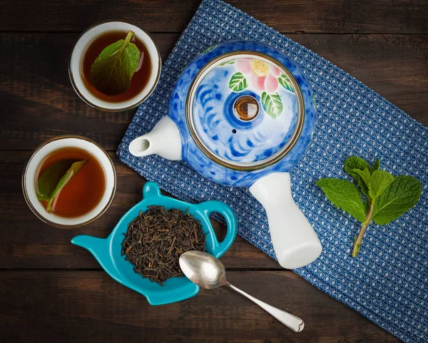 Whole leaf tea with teapot and two cups on towel and wooden background. Top view.