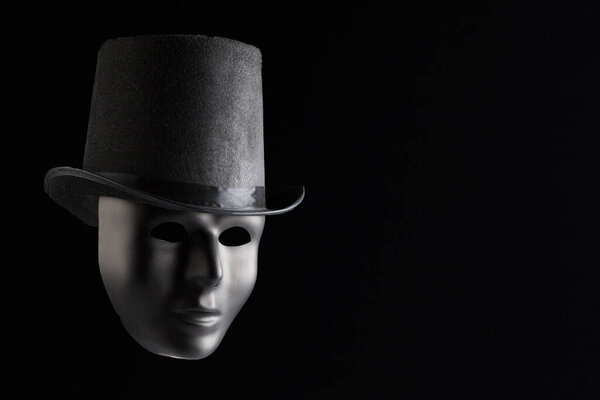 Черная маска лицо в черной цилиндр изолированы на черном фоне с копировальным пространством. Анонимность и тайна
