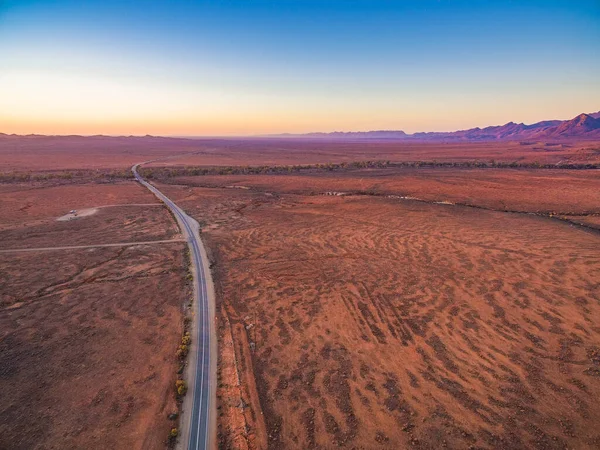 日没時に砂漠の赤い土地を通過する道路の空中ビュー — ストック写真