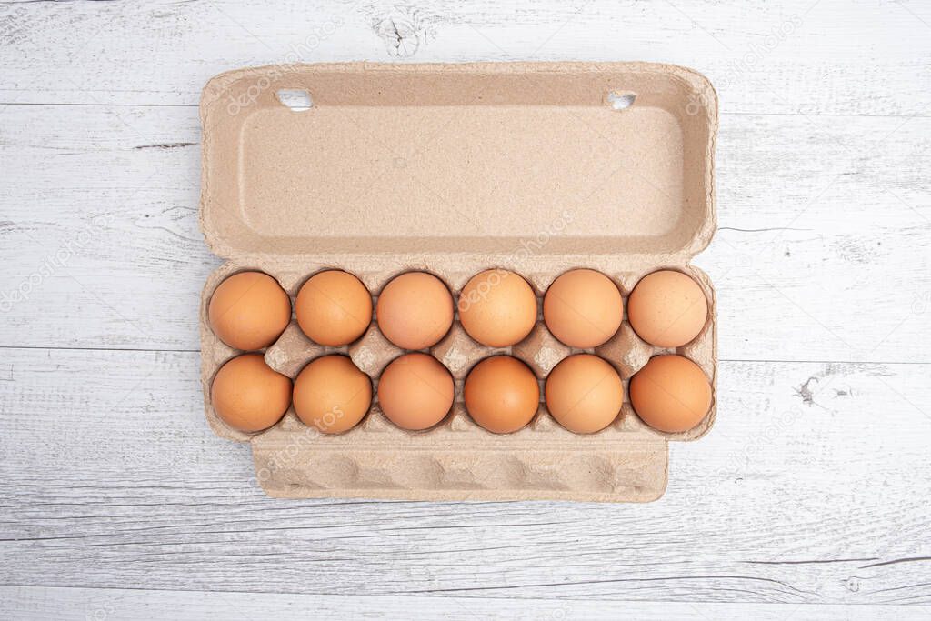 Dozen eggs in open cardboard packaging on white wooden table - top view with copy space