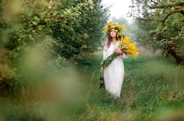 Junge schöne Frau in einem Kranz aus Wildblumen und einem langen weißen Nationalhemd — Stockfoto