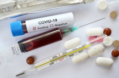 Tek kullanımlık şırınga ve test tüpündeki kan örnekleri COVID-19 için pozitif test sonuçları içeriyor. Tıbbi cıva cam termometresi 38.2 derece santigrat derece ve çeşitli tabletler gösteriyor.