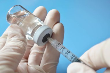 Plastik eldivenli bir tıp uzmanı açık mavi arka planda tek kullanımlık şırınga kullanarak tıbbi şişeden ilaç dozunu alıyor. Sağlık hizmetleri kavramı.