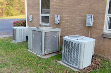 3 Air Conditioner Compressors outside commercial building with cutoff switches. clipart