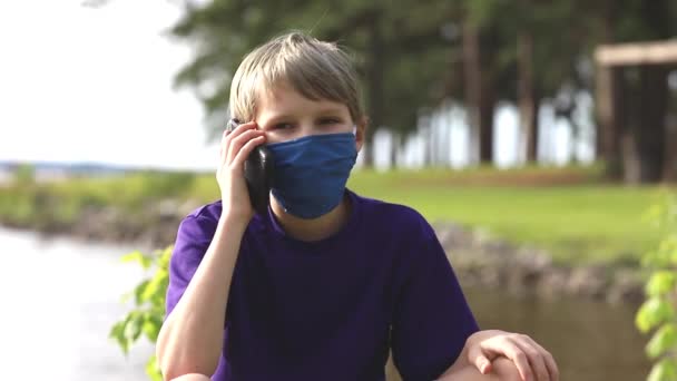 Niño hablando por teléfono celular mientras usa mascarilla facial durante la pandemia — Vídeos de Stock