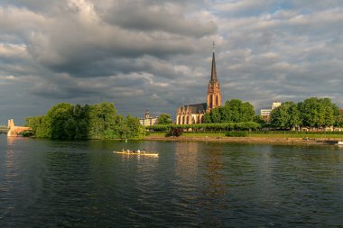 Frankfurt 'ta 4 adam ana nehirde kürek çekiyor. Arka planda bir kilise, inanılmaz bir ışık ve bulutlar var..