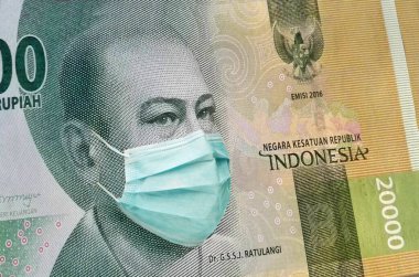 Endonezya 'nın 20.000 rupilik banknotu ve Endonezya' da bir tıbbi maske. Coronavirüs salgınının Endonezya ekonomisi üzerindeki etkisi.