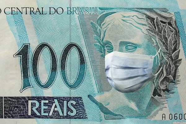                                        Tıbbi maskeli 100 Brezilyalı banknot. konsept. Brezilya 'da koronavirüs salgını. Coronavirüs salgınının Brezilya ekonomisine etkisi  