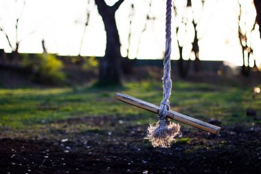 Çocuklar güneşin batışına karşı iplere sabitlenmiş salıncaklar