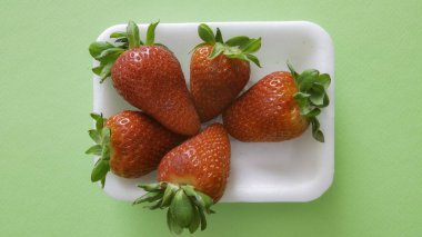 Yeşil kart arkaplanı ve sol altta yeşil yapraklı küçük kırmızı çilekler.