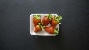 Siyah bir arka plan ve sol altta yeşil yapraklı küçük kırmızı çilekler.