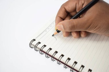 Beyaz bir arkaplan üzerine siyah kalemle beyaz bir not defterine yazı yazan bir kişi.