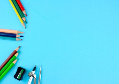 Farklı renklerde kalem kalemleri, siyah bir kalem açacağı ve bir kalem pusulayla açık mavi kağıt üzerine tutturulmuş.