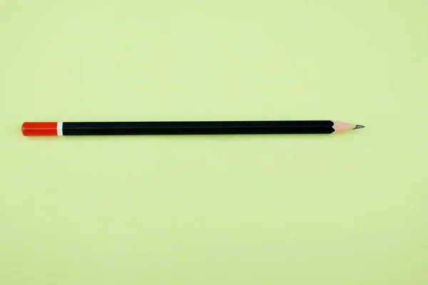 濃い黒の研ぎ澄まされた鉛筆が穏やかな環境の薄緑の紙の上に横たわっています — ストック写真