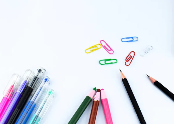 education materials arranged on a white background which includes five pens, two black pencils,three crayons and some paper clips.