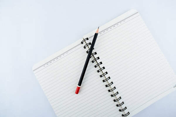 A dark black wooden pencil over a notebook on a isolated white background