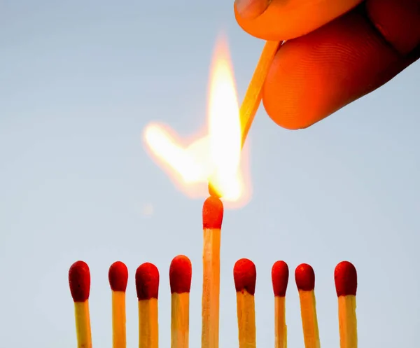 A person lighting a match stick with another match with fire holding in his hand over eight other matches