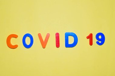 COVID-19 izole edilmiş açık sarı arkaplanda çeşitli renkli harf bloklarıyla yazıldı