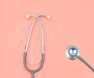 Tek bir normal steteskopun fotoğrafı. Pembe renkli boş bir kağıdın üstünde izole edilmiş.