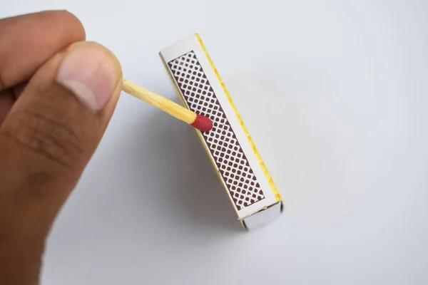 A person lighting a single match sticks by swiping the match with the box with his hand