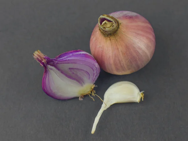 Yarım soyulmuş pembe soğan orta boy soyulmamış soğan ve siyah arkaplandan önce bir parça sarımsak.