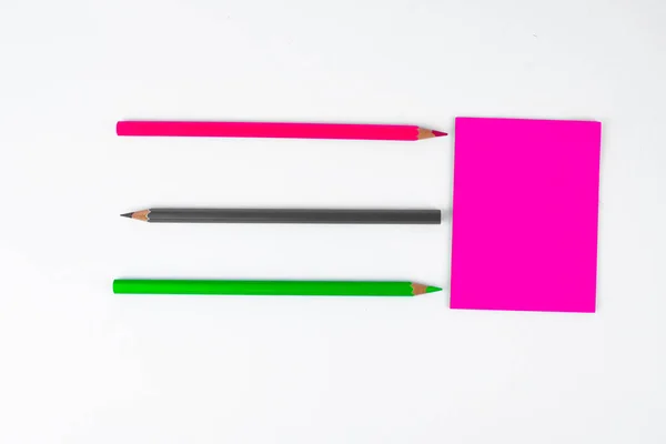 三支不同颜色的木制铅笔蜡笔指向粉红粘纸便条 — 图库照片