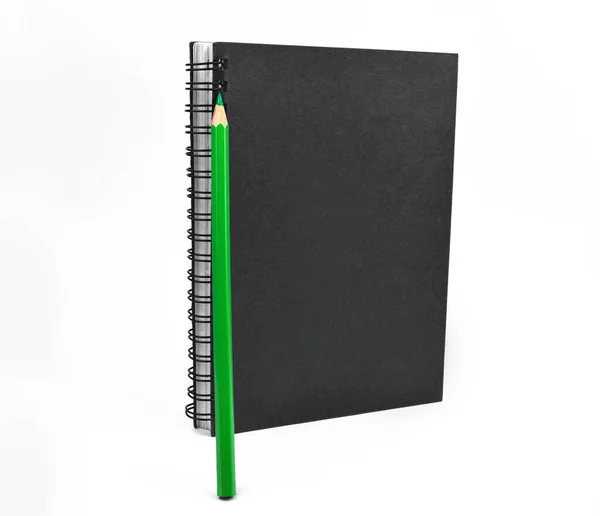 一支绿色的木制铅笔笔画在白色背景前的黑色记事本的前面 — 图库照片