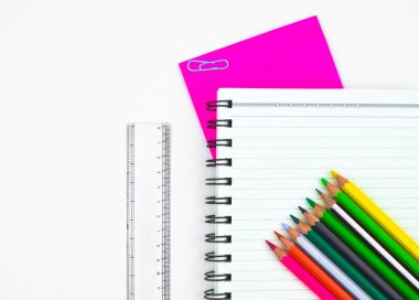 Beyaz arkaplandan önce farklı renk kalem, plastik ölçek, günlük ve pembe kağıt içeren çalışma materyalleri