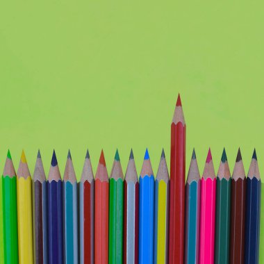 Boş bir açık yeşil kağıt arkaplana yerleştirilmiş farklı renkli kalem boyası satırı