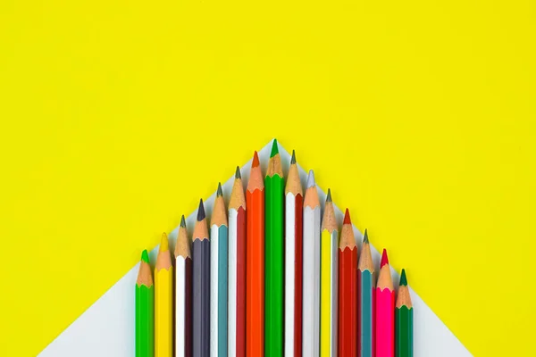 Pencil crayons of different color arranged as a pyramid row placed on a yellow paper background