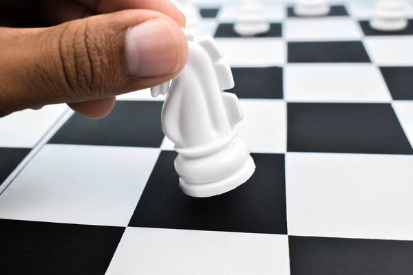 Один человек перемещает белого рыцаря с черного квадрата шахматной доски
