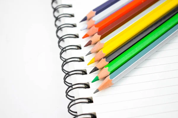白い紙の螺旋状のノートブックの上に置かれた異なる色の木の鉛筆クレヨン — ストック写真