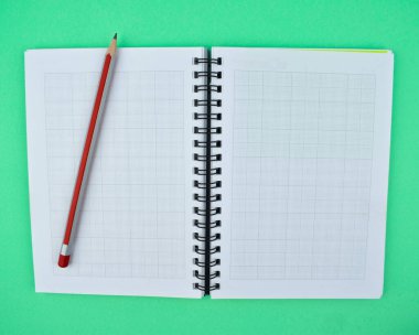 Kırmızı renkli tahta kalem. Beyaz sarmal kağıt defterin üstüne yerleştirilmiş.