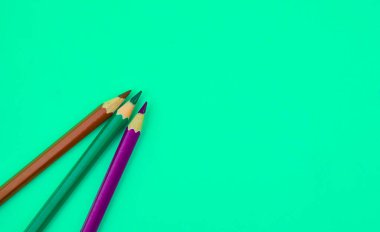 Açık mavi bir kağıdın üzerine üç farklı renkte tahta kalem yerleştirilmiş.