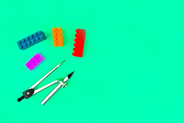 Building blocks and a silver color wood pencil attached to a pencil compass placed on a blue paper background