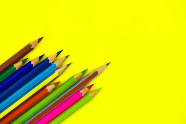 İzole edilmiş sarı bir arka fonun üzerine bir sürü farklı renkte tahta kalem yerleştirilmiş.