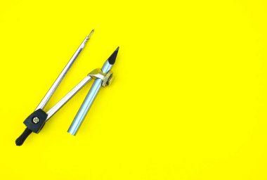 Sarı kağıt arka planda gümüş renkli tahta kalem pastel boyaya bağlı bir pusula.