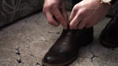 Bir adam kanepeye oturur, gri pantolon giyer, siyah ayakkabılar giyer.