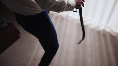 Beyaz gömlekli bir adam otel penceresine yaklaştı ve kahverengi bir deri kemer taktı.