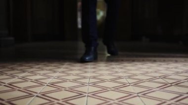 Deri ayakkabılı bir adam karanlık bir koridor boyunca yürüyor.