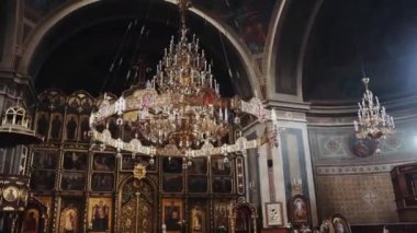 Tavandan sarkan bir sürü sarı ampulü olan büyük altın bir avize ve büyük bir sunakla karanlık kasvetli bir kiliseyi aydınlatıyor.