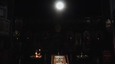 Bir kutsal ikon çok karanlık bir kilisede duruyor, ve yukarıdan gelen parlak bir ampulle aydınlatılıyor, yanında iki yüksek şamdan var, mumlar yakılıyor, yakın çekim, ön görüş..