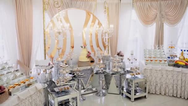 Un grand, beau, vitreux, lumineux, buffet avec beaucoup de boissons alcoolisées, collations sucrées et de viande, attend les clients pour une journée festive. Il y a un grand gâteau de mariage à plusieurs niveaux sur un beau stand 