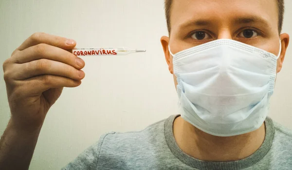 A masked man measures his temperature on a thermometer. Isolated on a light background.Coronavirus. 2020Novel Coronavirus (2019-nCoV). 2