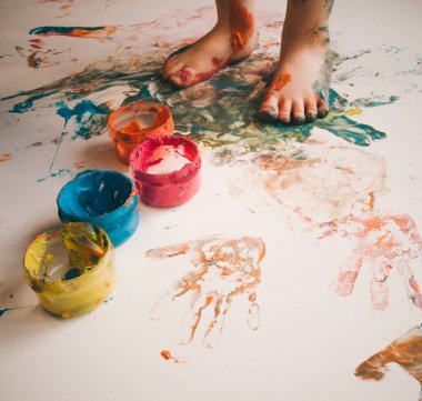 Çocuk beyaz arka planda boyalı ayaklarıyla oynar ve çizer.