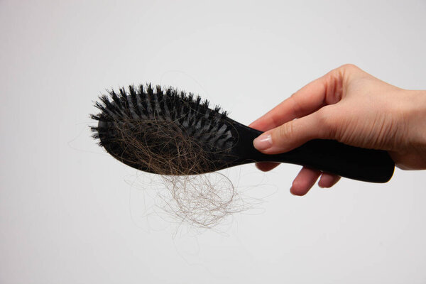 A girl holds a comb with fallen hair in her hand on a white background. The problem of hair loss. For the presentation of the lifestyle and means to care for hair and scalp.