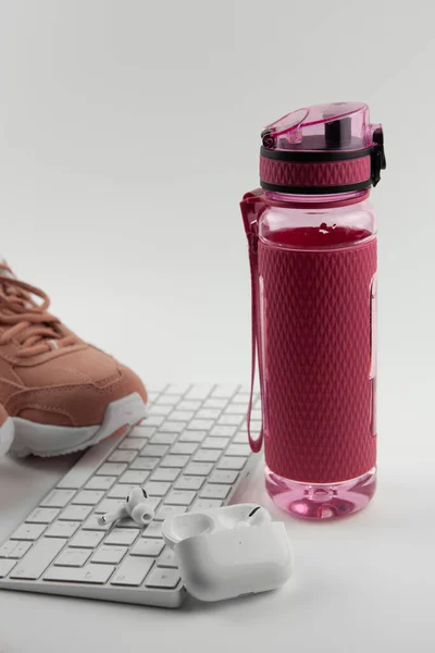 Beyaz bir klavye ve kablosuz kulaklığın yanında pembe plastik bir su şişesi. İnternetteki spor