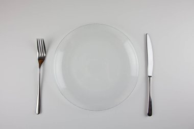 Şeffaf plaka, metal çatal ve beyaz arka planda bıçak. Masa ayarı. Yemeklerin ve restoranların sunumu için..