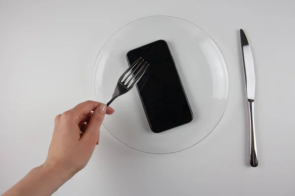 Şeffaf bir tabakta telefon olan demir çatal ve bıçak. Telefondaki bilgi tüketimi kültürü. Netiquette.